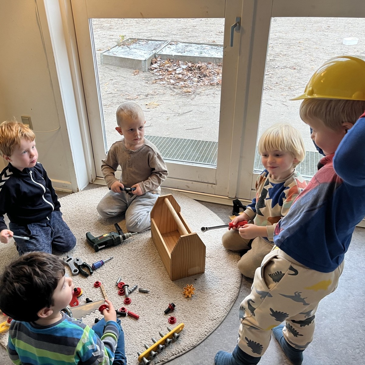 Fem drenge fra børnehaven sidder i en cirkel på gulvet og leger med værktøj.