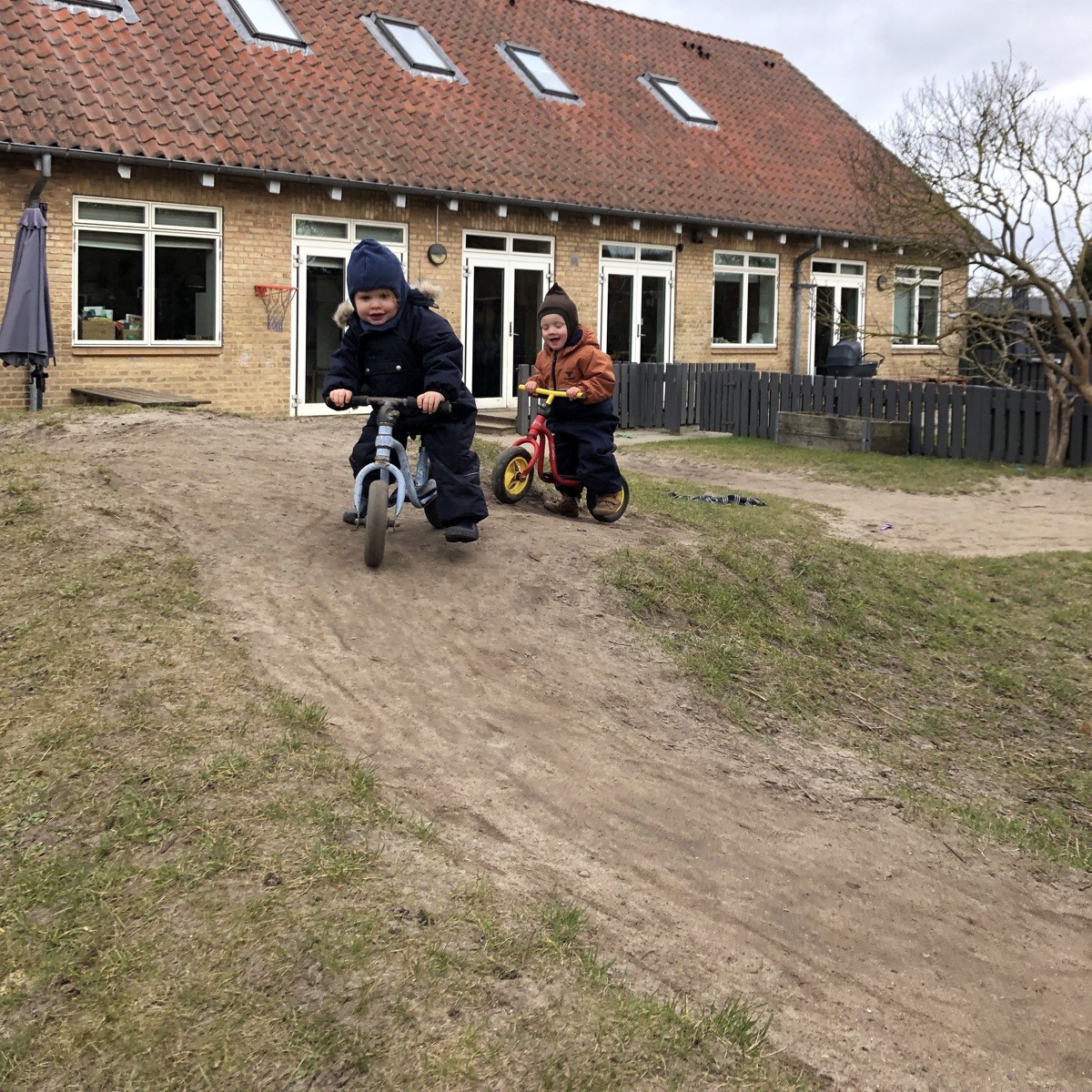 To børn kører på cykel ned af bakken på legepladsen.