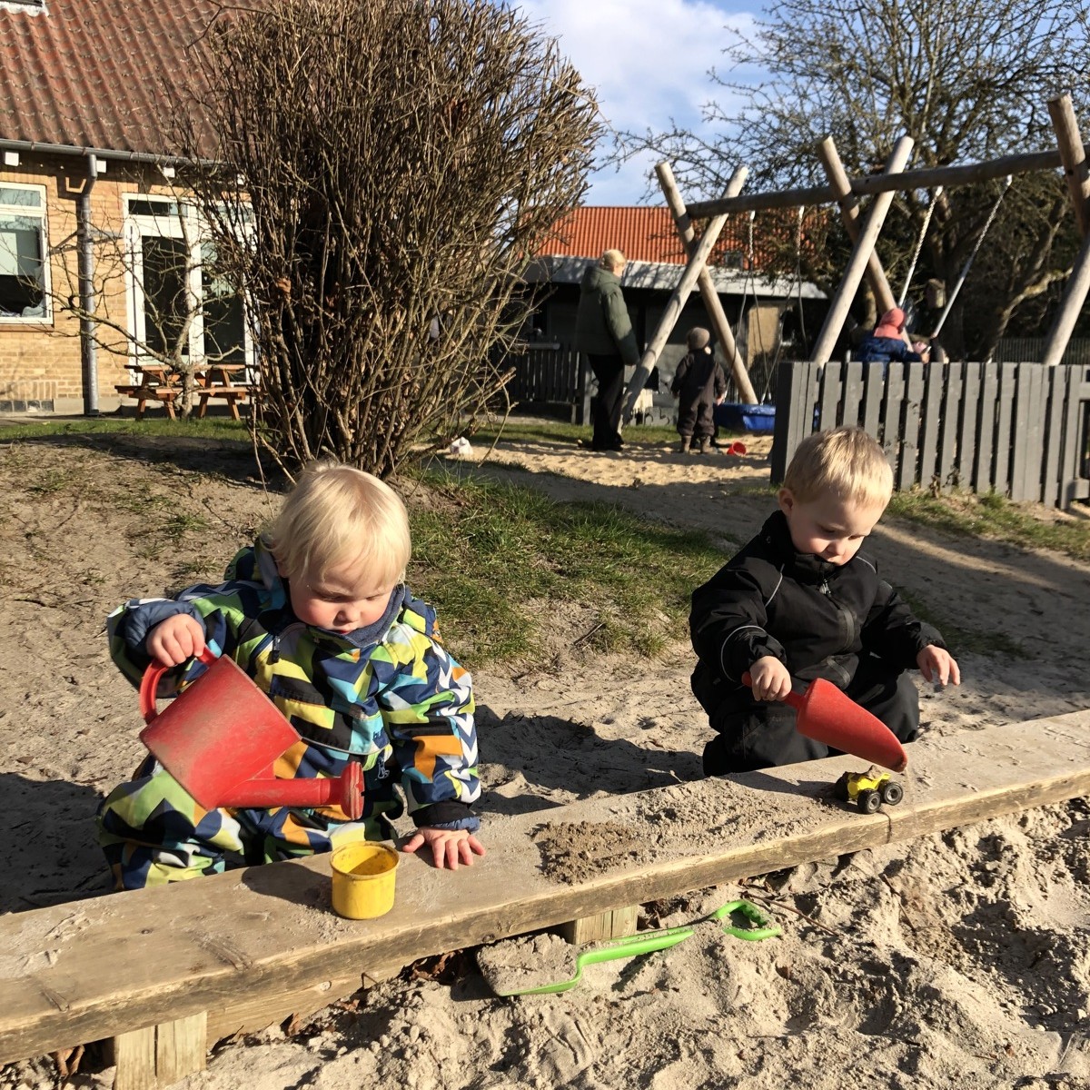 To drenge fra vuggestuen leger i sandkassen på legepladsen.
