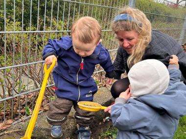 To børn og en voksen er på jagt efter insekter på legepladsen.